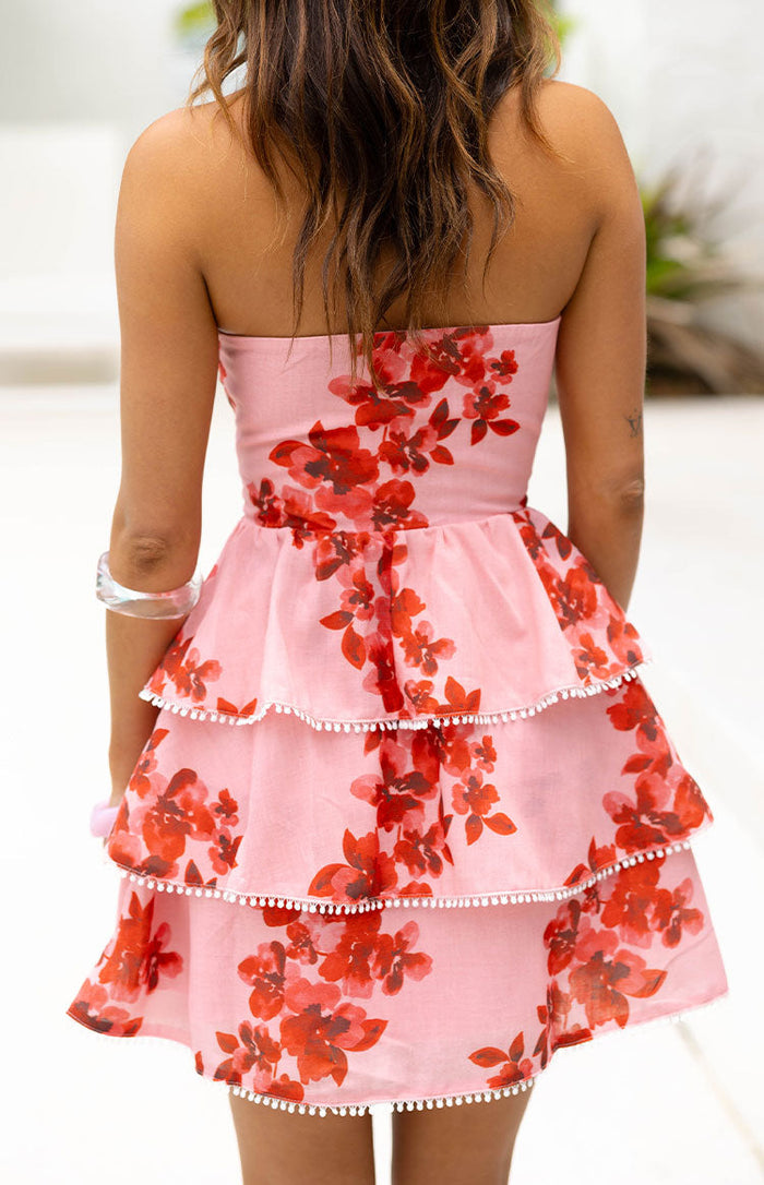 Rear view of a pink floral strapless mini dress with tiered ruffles and white pom-pom trim