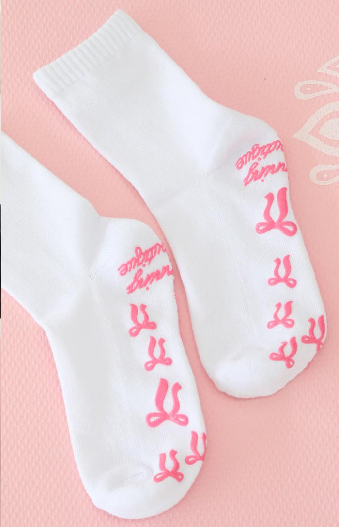 Soles of white yoga socks with pink bow-shaped grips and pink lettering on the arch