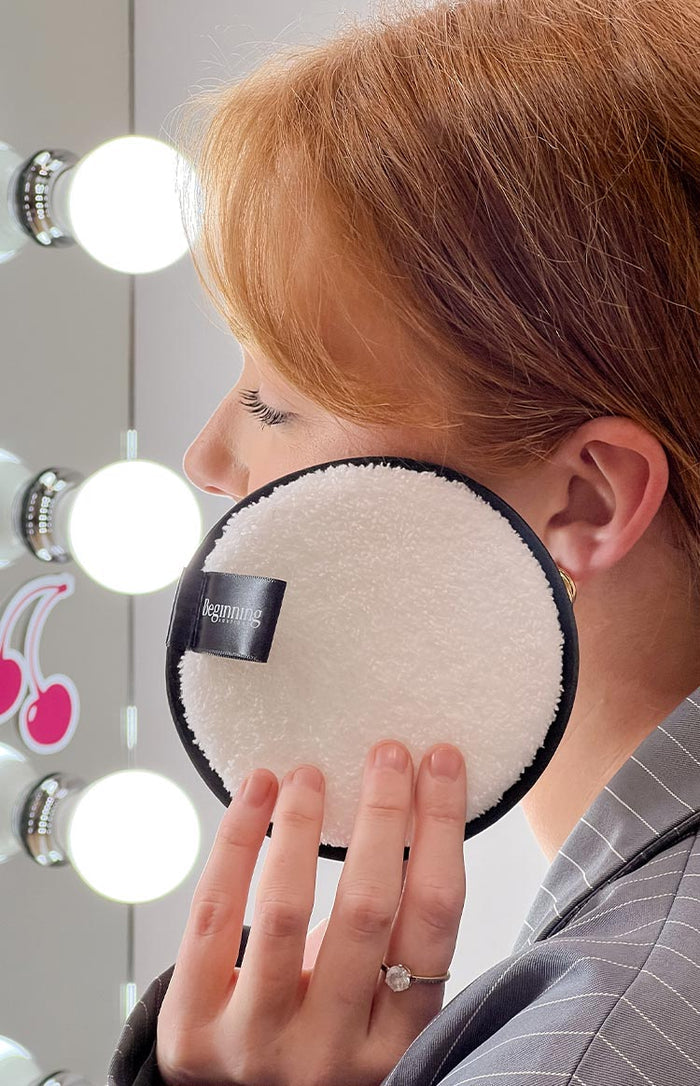 Close-up of the soft white texture of a reusable face wash pad, with black trim and a black fabric tag