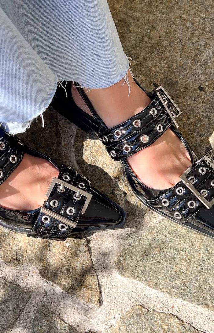 Close-up of the black patent pointed flats with two buckled straps adorned with silver eyelets