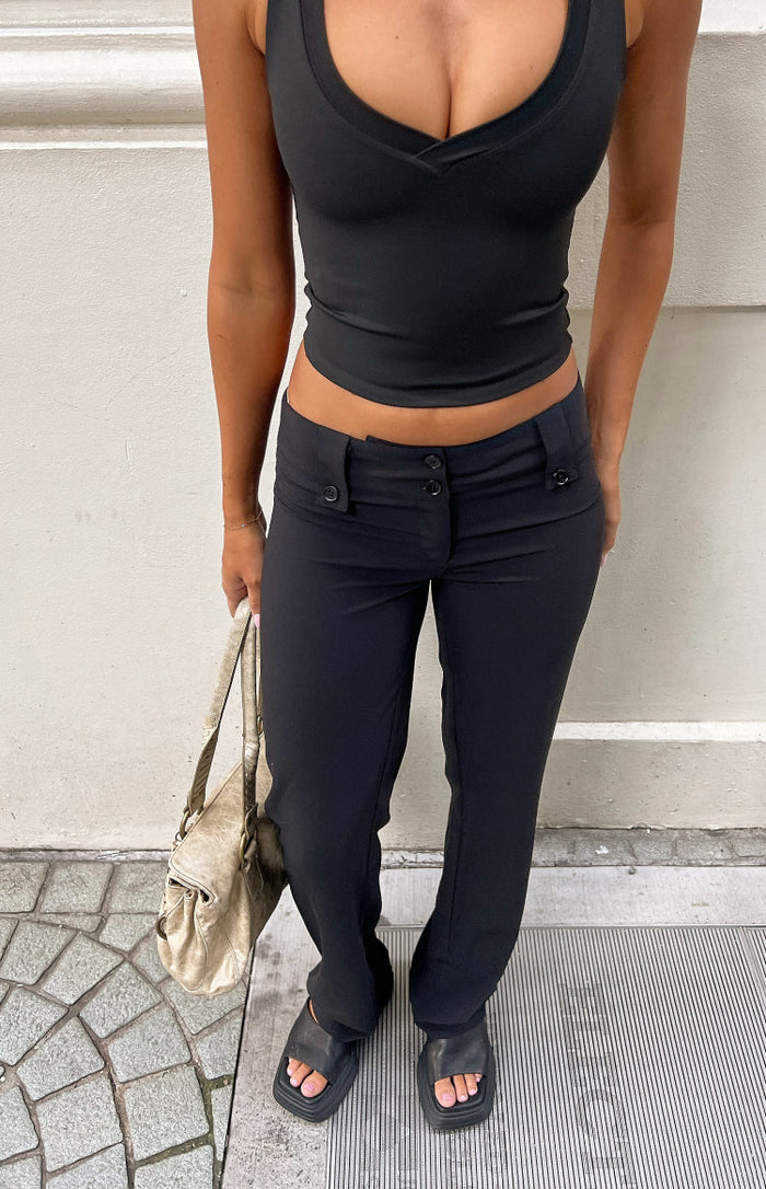 Close-up of black low waist pants showing the button fly and side tab details with a straight leg fit