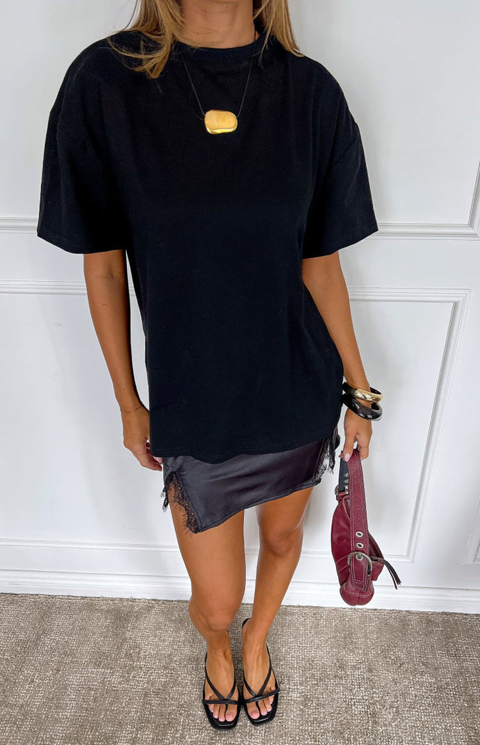 Front view of a black satin mini skirt with an asymmetrical hem and delicate black lace trim