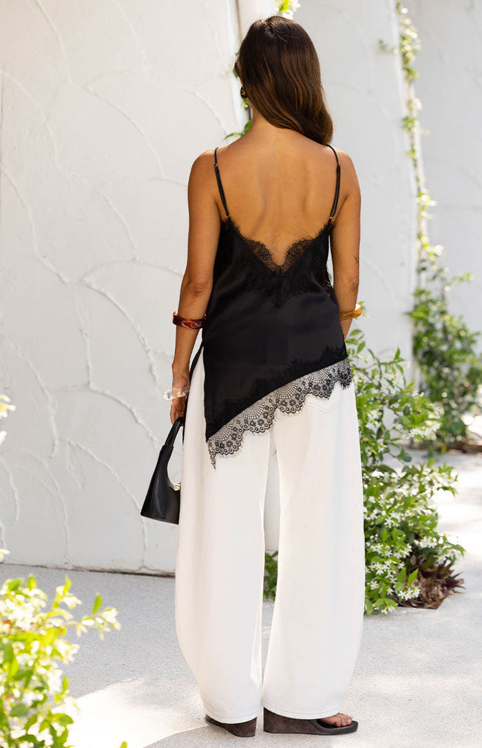 Rear view of a black satin asymmetrical top with a low V-neck back and lace trim along the neckline and hem